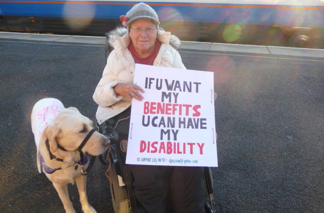 Woman holding 'If u want my benefits u can have my disability' placard