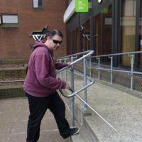 A blind man using a cane approaches a Job Centre